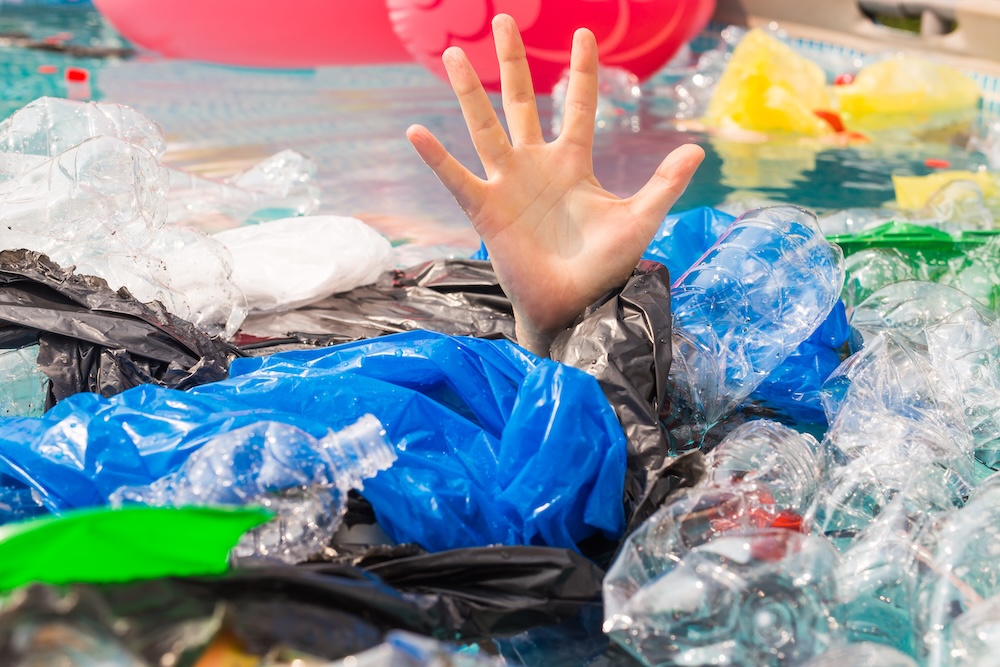 person under pile of plastic with single hand reaching out