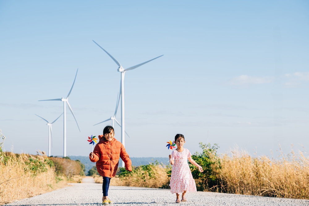 two young children running with wind turbines behind them