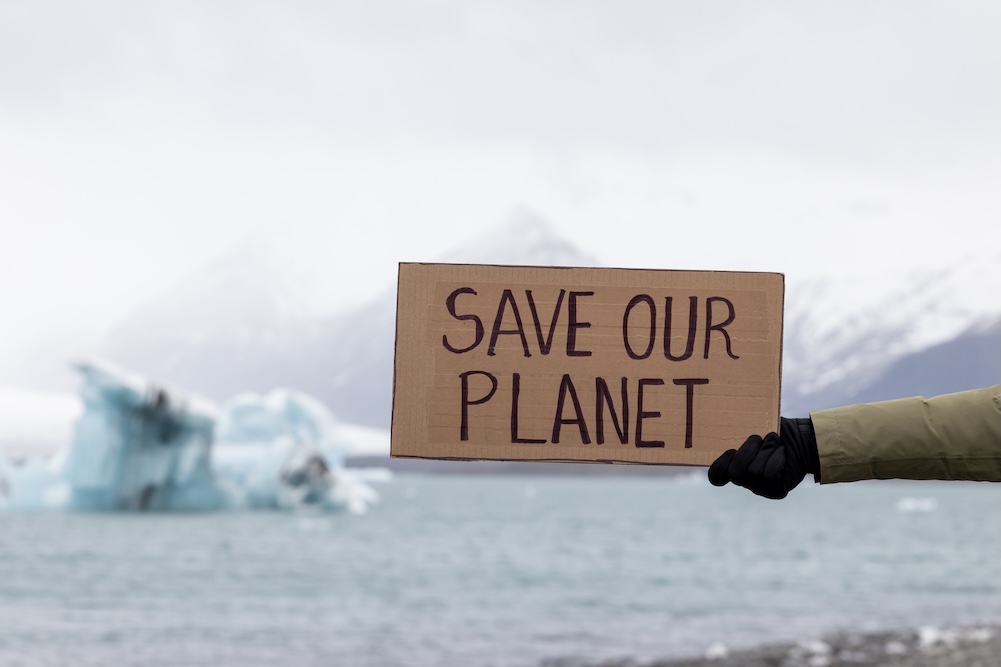 Person holding sign that says save our planet with melting ice in the background
