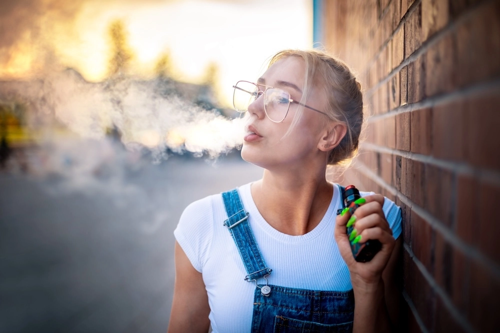 Young woman vaping outside blowing vape into the air