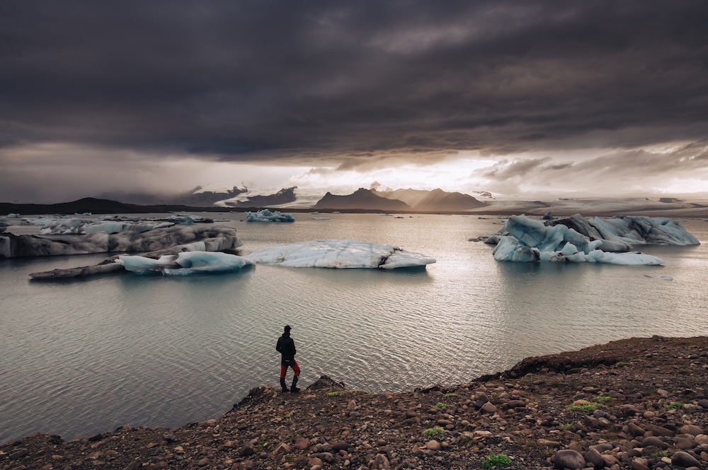 Man at a distance standing near ocean with ice melting