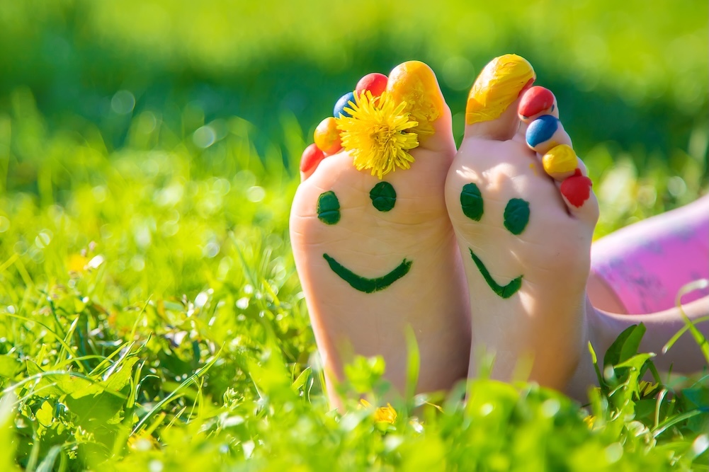 Person laying in the grass with feet painted with smiley faces