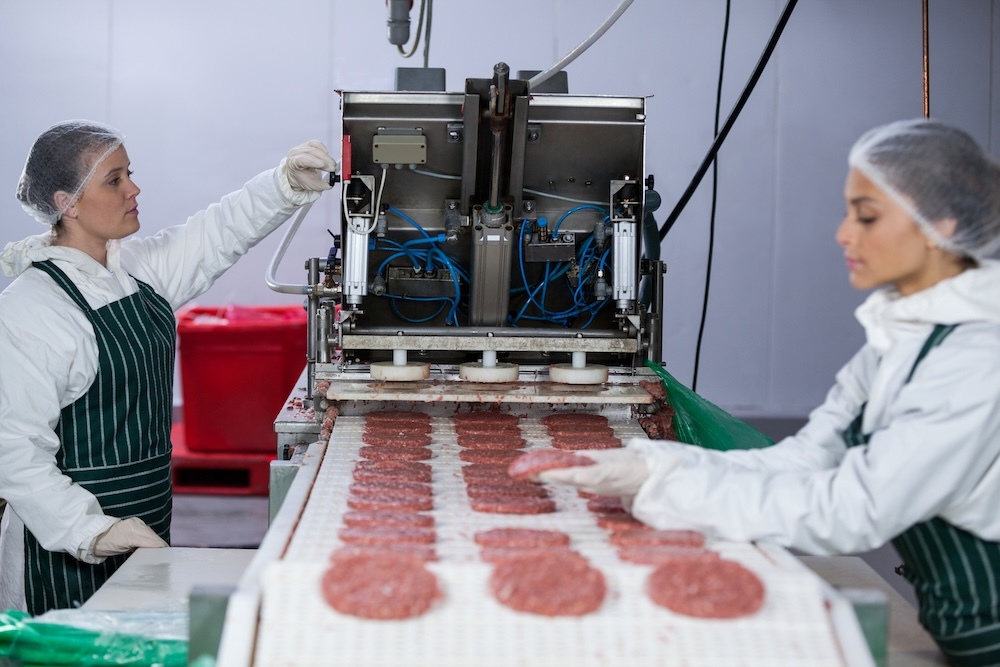 Two women processing hamburger patties on a machine