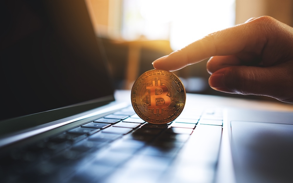 A person's finger on a bitcoin sitting on a laptop
