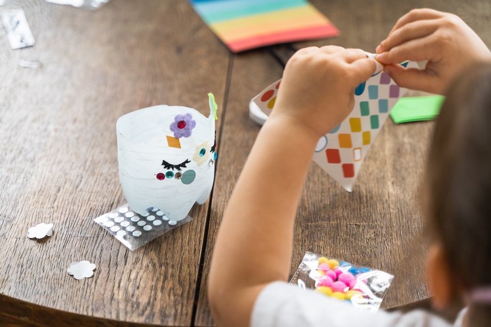 child making arts and craft using stickers and plastic bottles