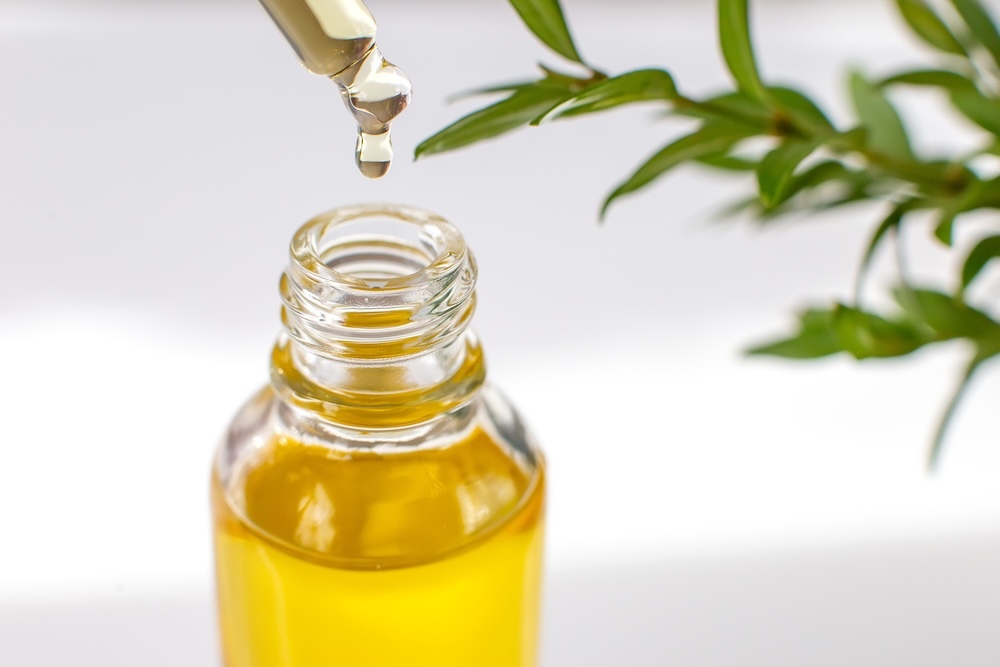 close up bottle of tree tea oil with a plant in the back