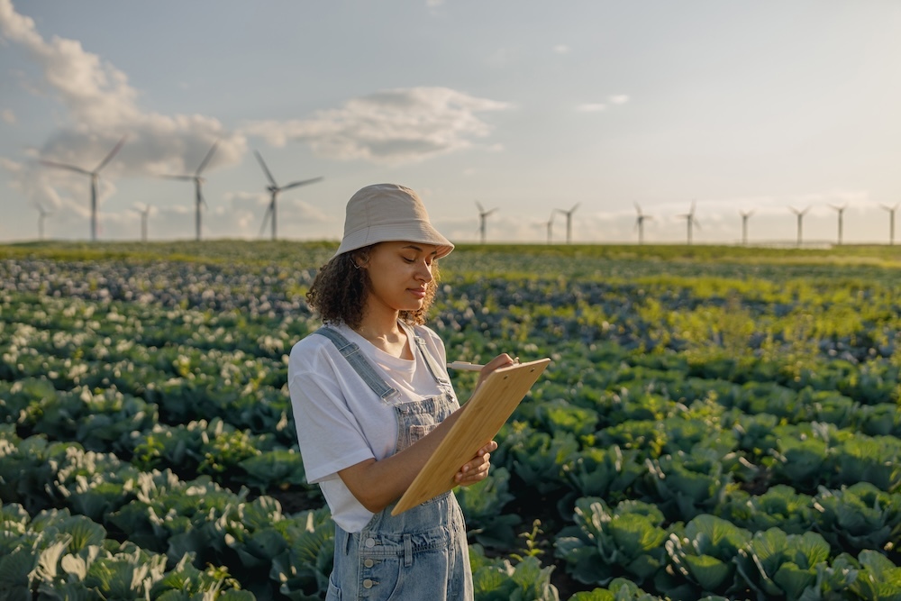woman taking notes in a field with crops and wind turbines