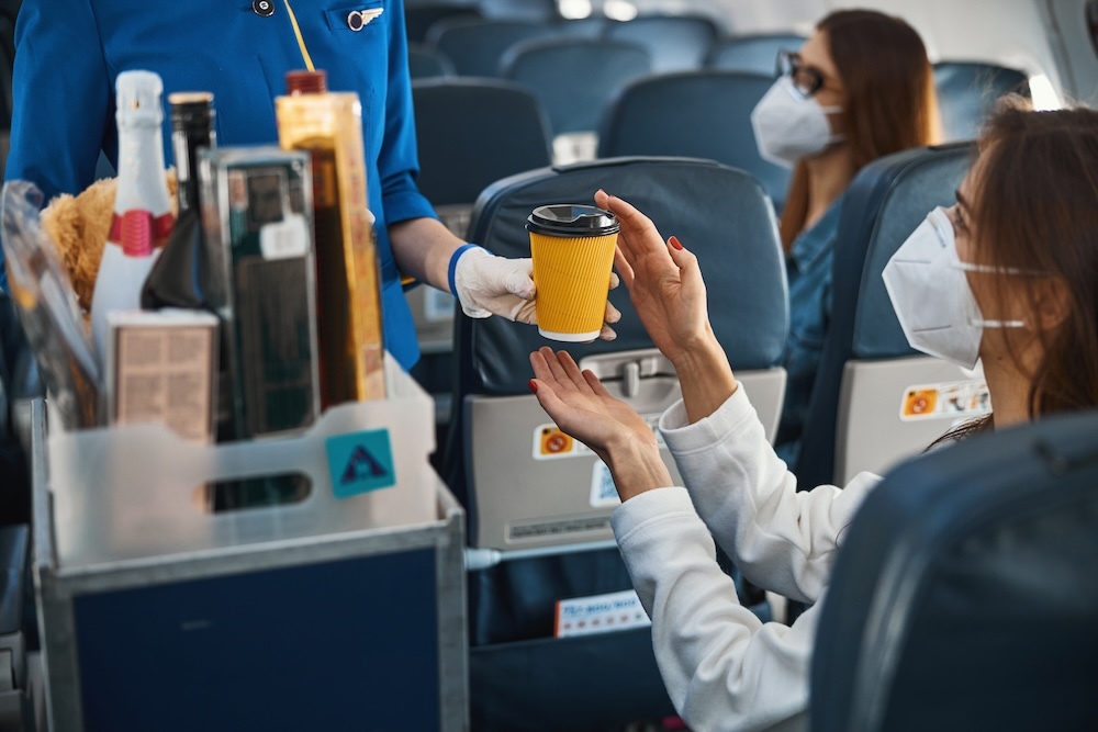 flight attendant handing passenger a paper cup with black plastic lid