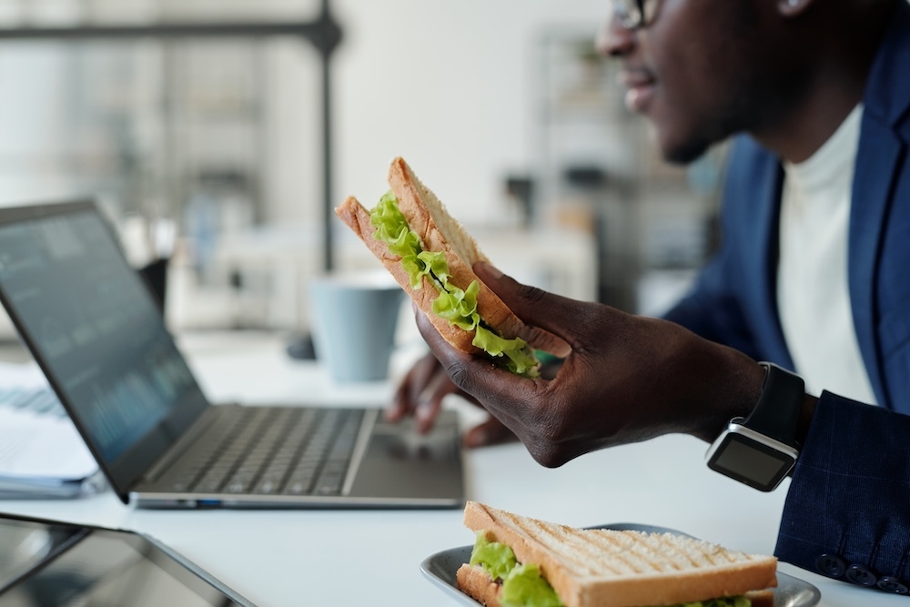 businessman eating a sandwich while working at his laptop from home