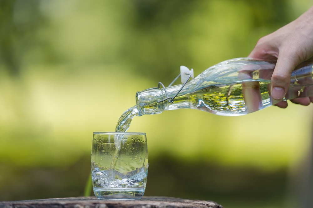 person pouring water into a glass against a green nature background
