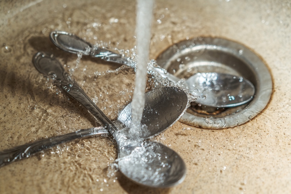 spoons with hard water coming out of faucet into sink