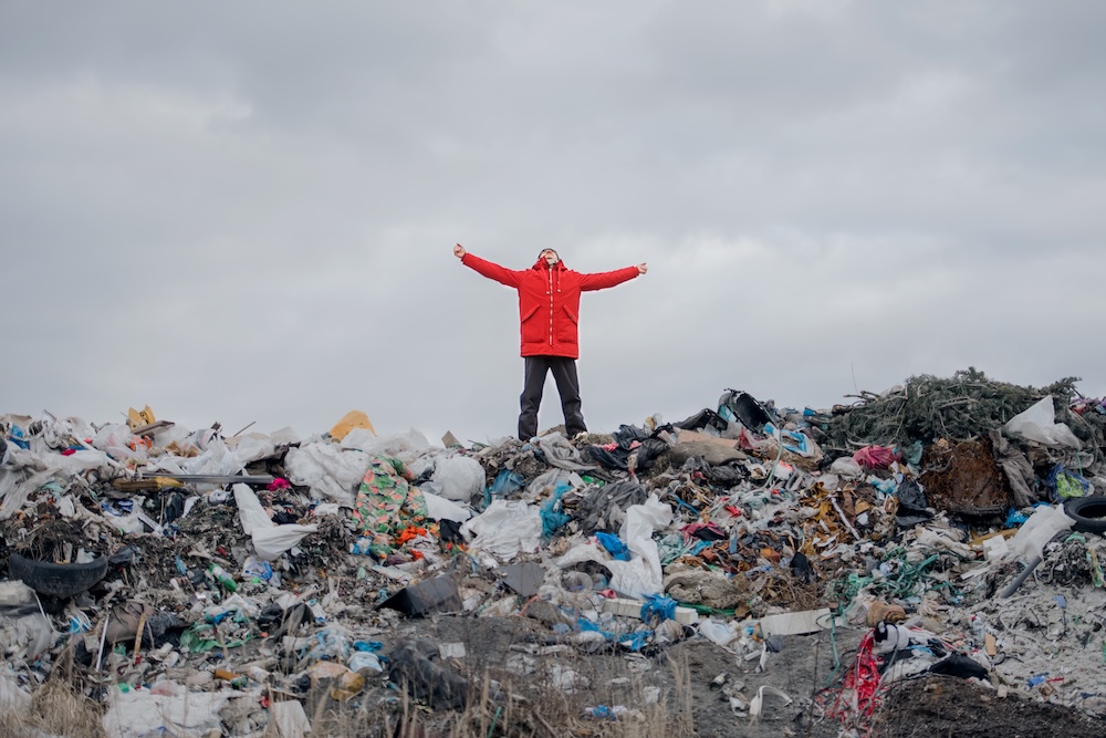 man standing on landfill pile frustrated with arms out