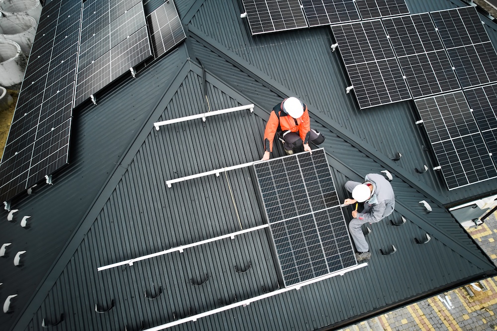 workers installing solar panels on top of a house
