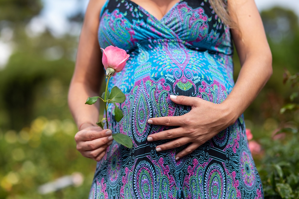 pregnant woman holding a flower standing in nature