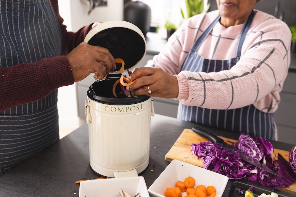 two people putting in vegetable peels in compost