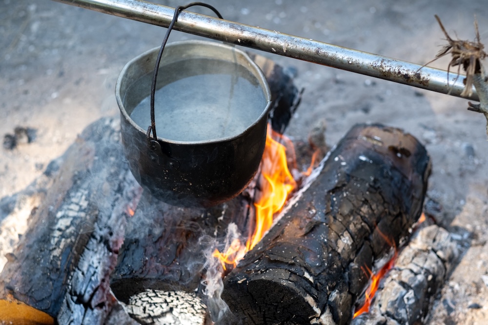 water in a cast iron pot over a campfire