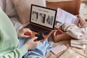 person shopping online with clothing unpacked in a box int he background