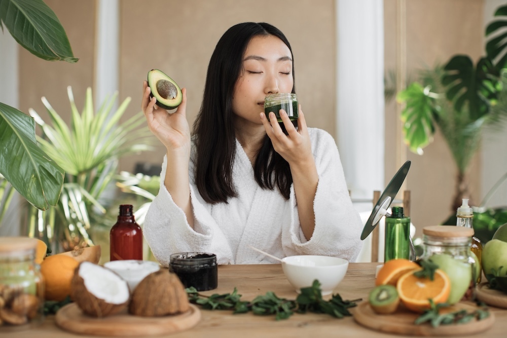 woman smelling natural beauty products holding an avocado