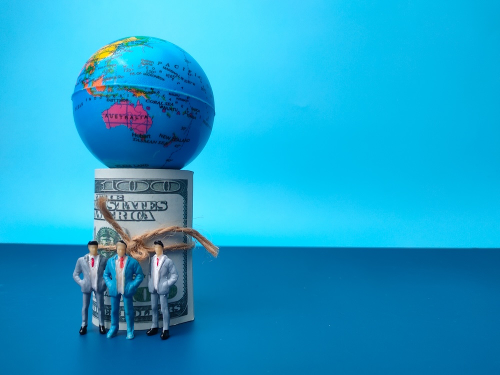 people standing around rolled money with earth on top