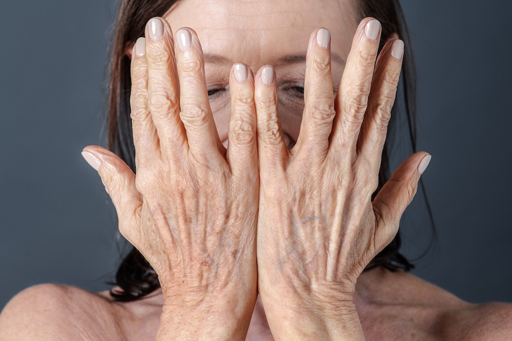 senior woman with aging hands covering her face