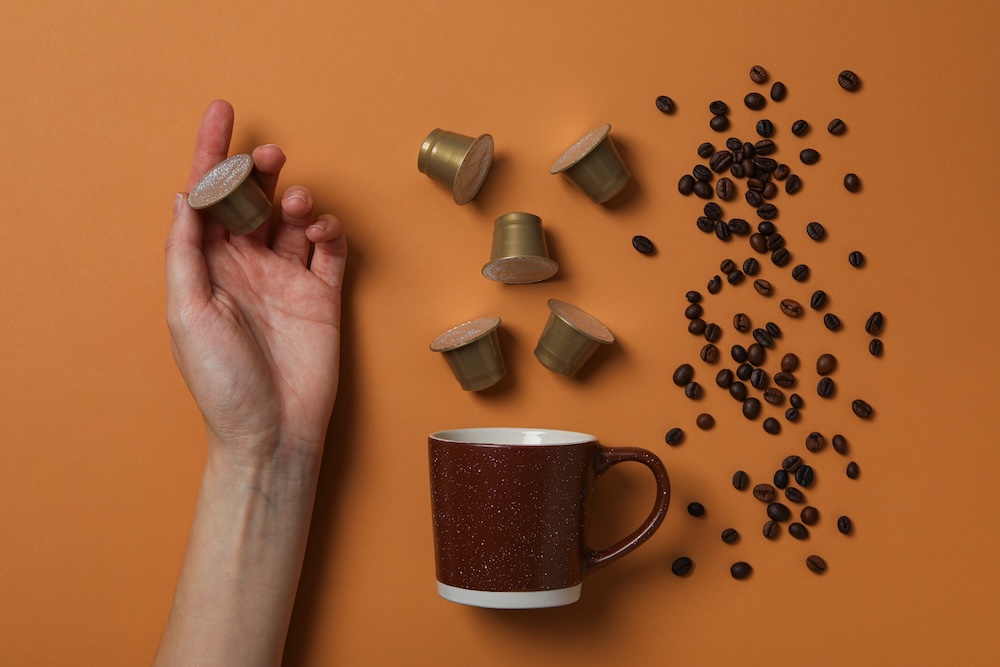 Hand holding coffee pod next to a coffee cup and coffee grounds
