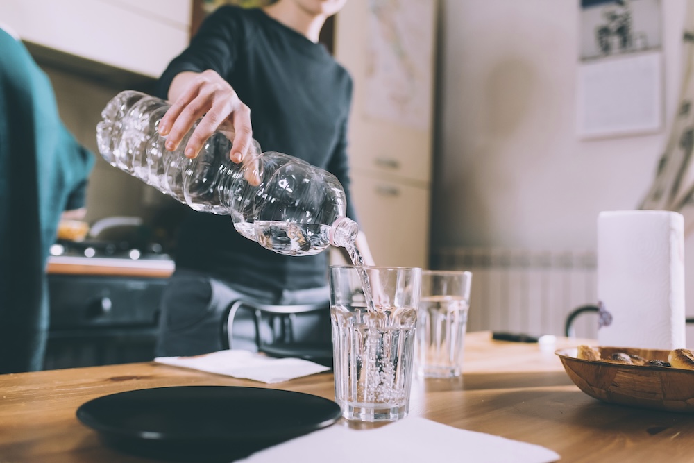 Young person pouring water from a plastic bottle into a glass