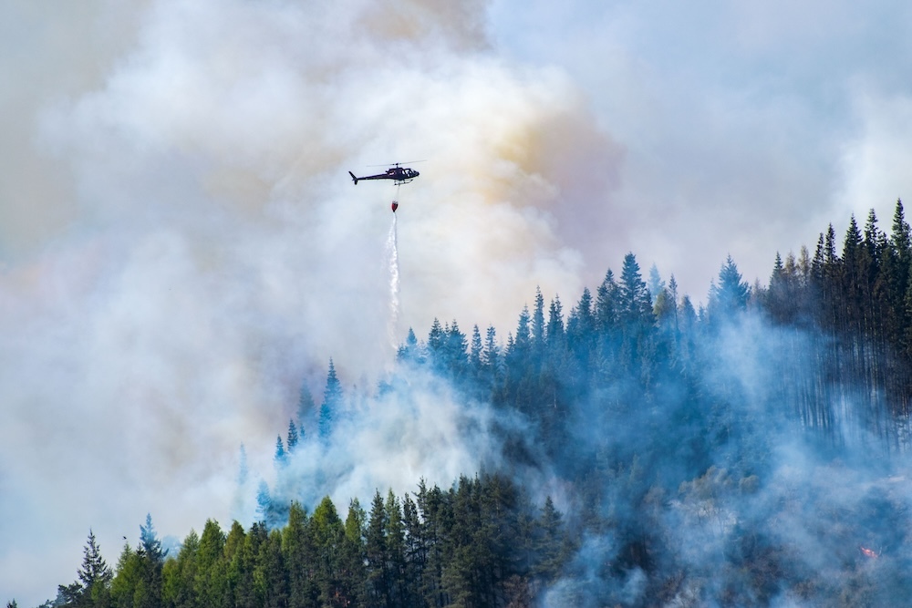 helicopter flying over wildfire dropping water