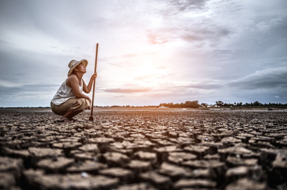 Woman kneeling looking at a land of drought