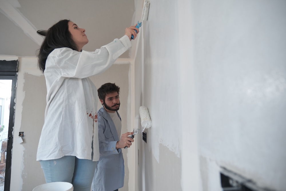young couple painting walls white with rollers