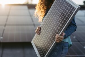 Woman carrying a solar panel with solar panels in the background