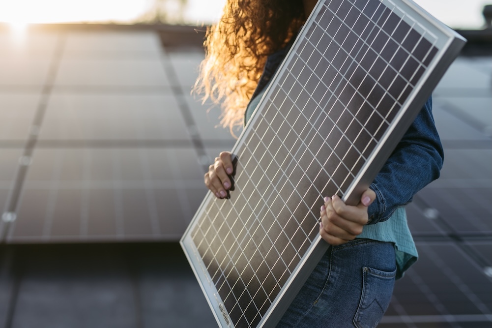 Woman carrying a solar panel with solar panels in the background