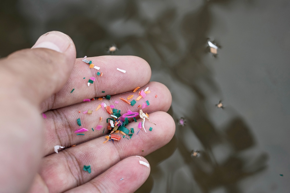 Microplastics on a persons hand falling into water