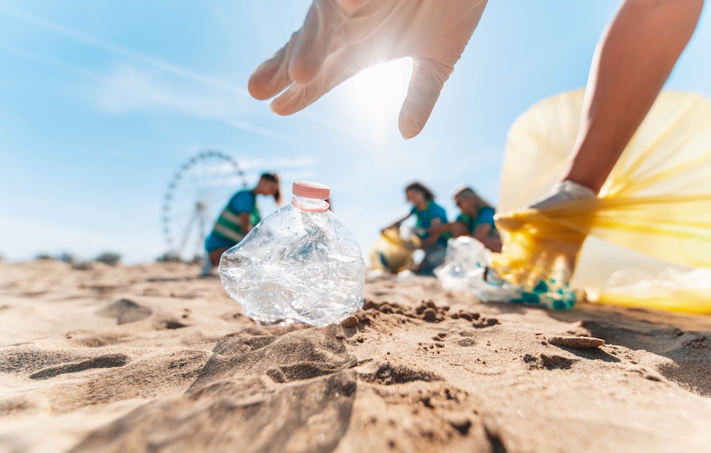 Hand picking up a plastic bottle off the beach