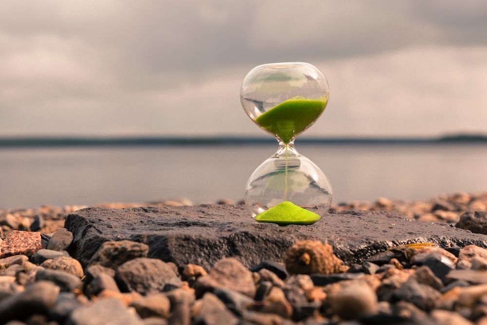 hourglass sitting near a lake with green sand pouring out