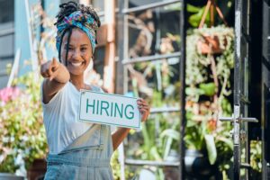 woman outside of garden shop holding sign says hiring