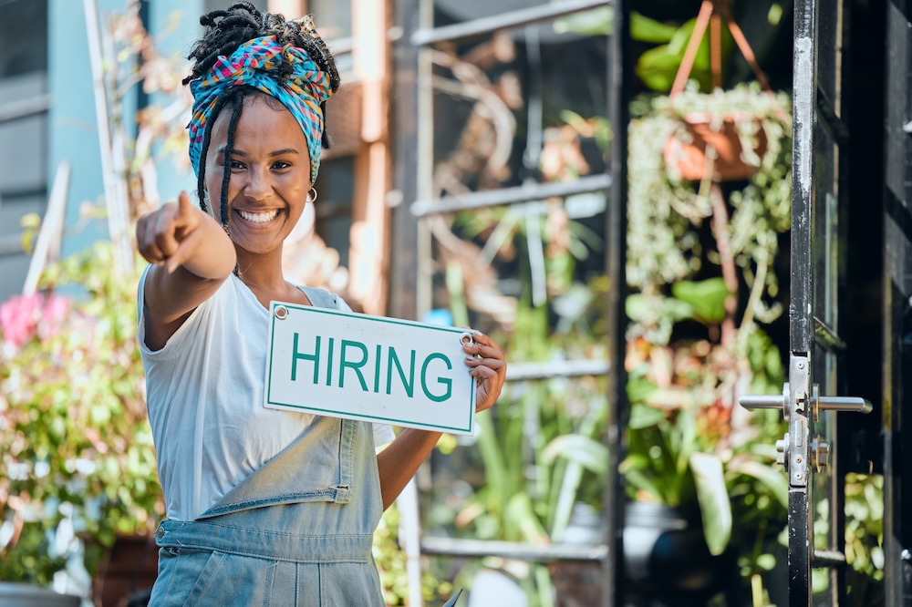 woman outside of garden shop holding sign says hiring