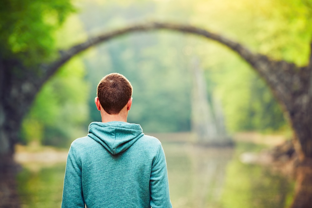 Man standing in nature admiring greenery and a bridge