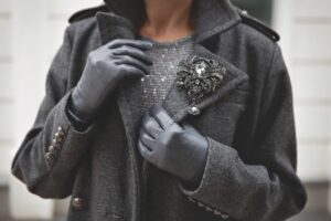 Woman wearing a grey jacket, black gloves, and a silver brooch