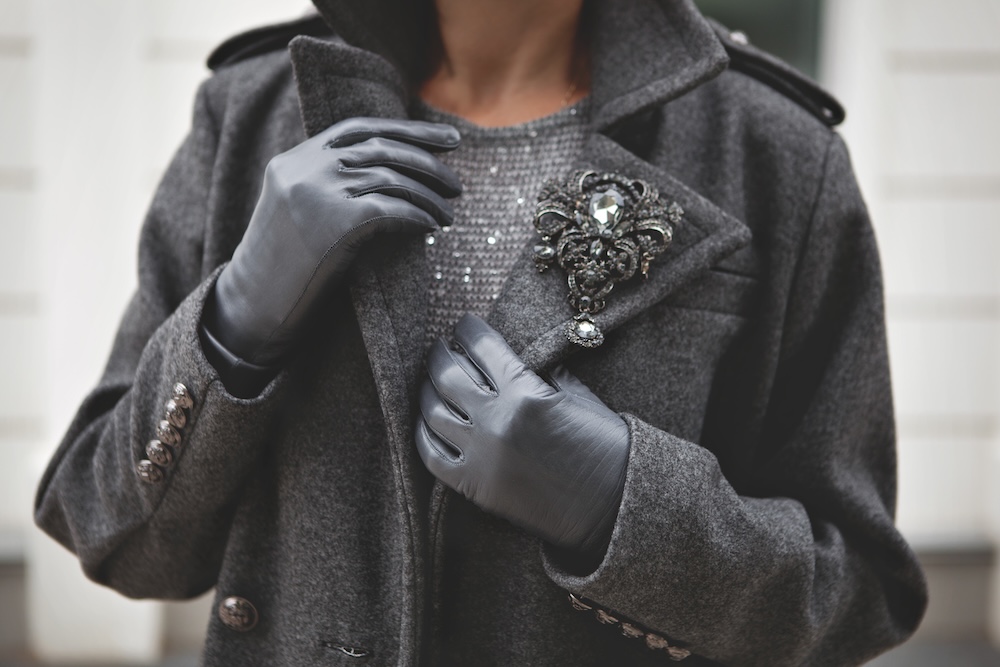 Woman wearing a grey jacket, black gloves, and a silver brooch