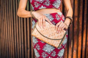 Woman in a floral outfit holding a natural fiber handbag
