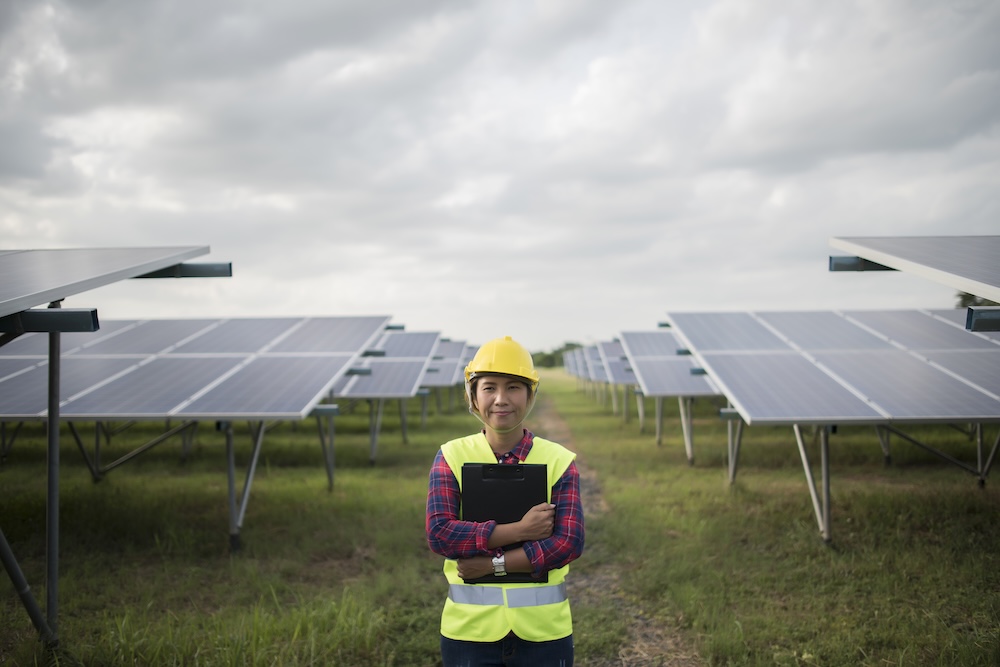 Female engineer standing between solar panels on solar farm