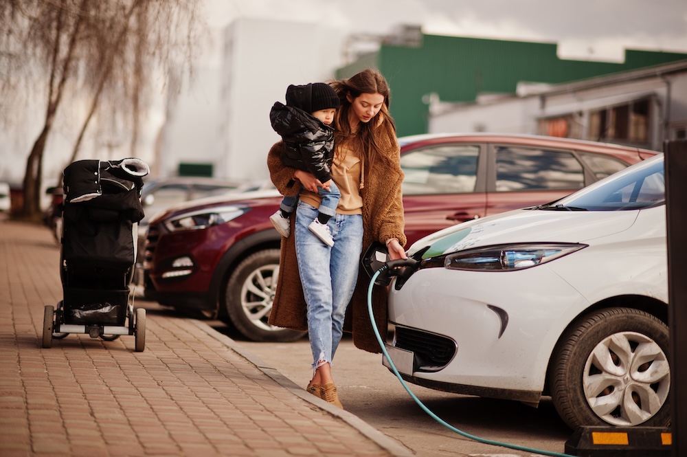 Young mother holding child while charging her electric car