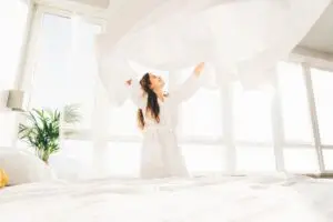 woman making her beds fluffing her bed sheet