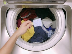 person loading laundry into machine and adding powdered detergent
