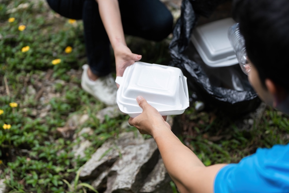 two people picking up trash putting styrofoam food containers in garbage bag