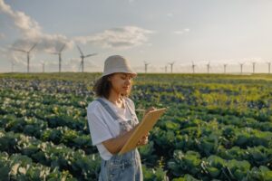 woman taking notes in a field with crops and wind turbines