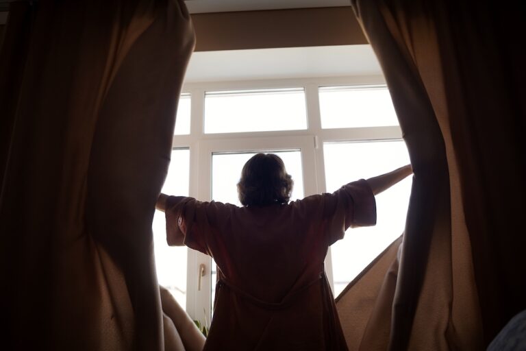 woman opening up black out curtains in morning