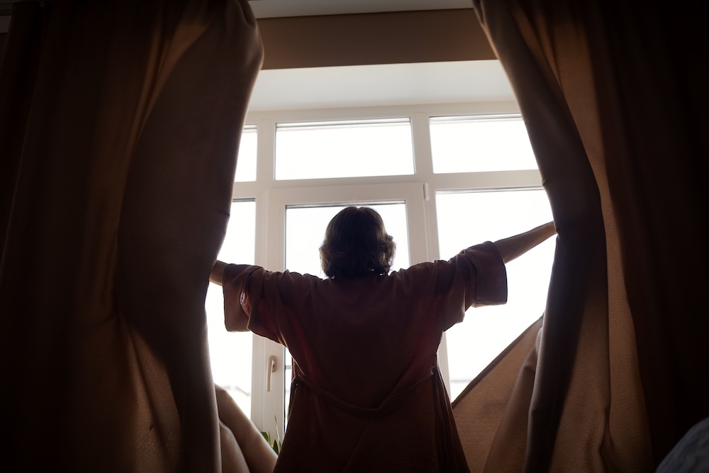 woman opening up black out curtains in morning