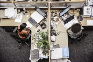two people sitting at their desks with clutter and waste around them