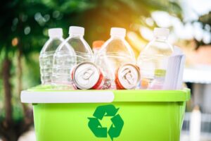 consumer recycling bottles and cans in a green bin